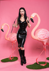 lovely fetish woman in bdsm clothes posing on pink background with flamingo birds