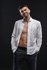 Charismatic attractive man in a unbuttoned white shirt hands in his trouser pocket isolated on a black background.