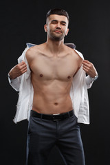 Charismatic sexy man takes off white shirt isolated on black background.