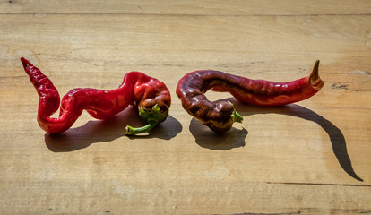 Two cayenne peppers on a wooden block next to each other with a long shadow