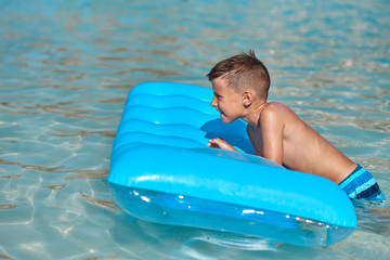 The portrait of cute European boy. He is laying on the blue inflatable floater, enjoying his holidays and smiling.