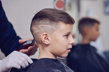 ber making a haircut to a cute European boy using cutting machine.