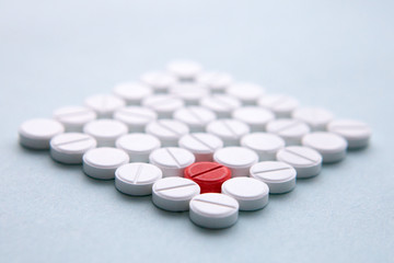 Top view of a pile of white medicine pills on a white surface. One tablet of red medication. Vaccine concept 