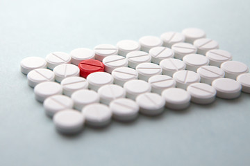 Top view of a pile of white medicine pills on a white surface. One tablet of red medication. Vaccine concept 