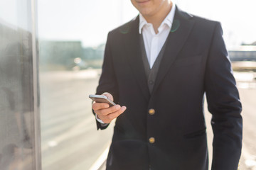 Young and Casual Businessman Using Smartphone while Walking Outside of Office Building