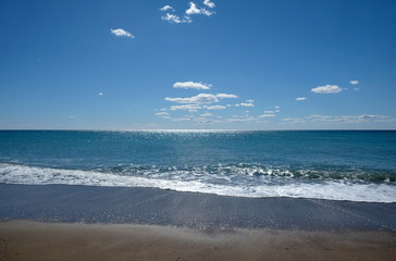 Beautiful sieside landscape with calm sea surf with waves runs to the empty sandy beach and and sun reflecton on water on skyline in sunny summer day