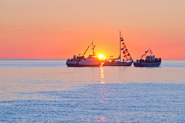 Silhouettes of three ships against the setting sun.