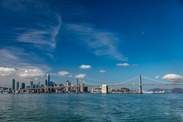 Mostly blue skies fill the picture of the San Francisco skyline on the left and the bay bridge on...