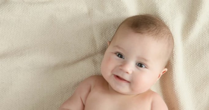 Top view of the baby looking in the camera and smiling, close up 4k shot. A cute little baby is look and smile. Babyboy looks around and smiles and laughs, view drom above