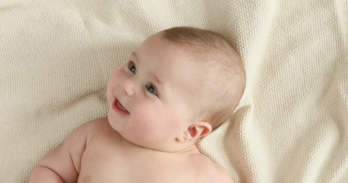 Top view of the baby looking in the camera and smiling, close up 4k shot. A cute little baby is look and smile. Babyboy looks around and smiles and laughs, view drom above