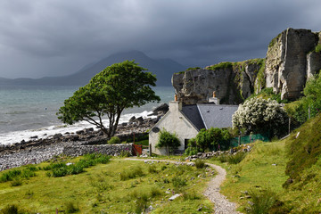 House under cliff at Elgol beach with Red Cuillin Mountains under clouds at Loch Scavaig Scottish Highlands Isle of Skye Scotland UK