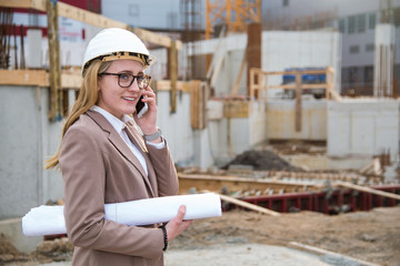 Frau als Architektin mit Helm, Bauplan, Plänen telefoniert auf einer Baustelle mit Kran