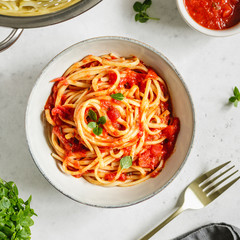 Top view of traditional pasta with tomato and Greek basil sauce in a ceramic bowl on a white table.
