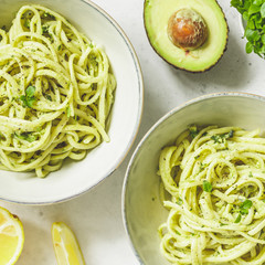 Top view on pasta with avocado and Greek basil sauce in a ceramic bowls on a white table. Dinner or lunch for two.