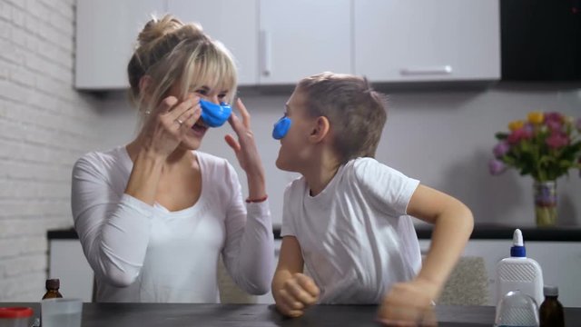 Cute little boy with adult mother laughing at each other making funny faces with sticked blue slime. Joyful familly parepared handmade slime and and enjoyed together