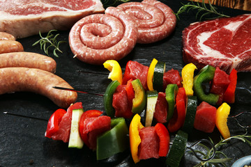 Assorted delicious raw meat with vegetable on a barbecue with t-bone steak, sausages and meat...