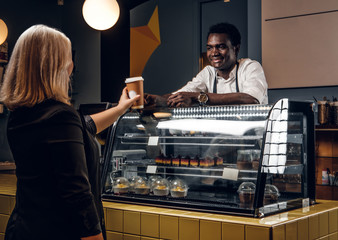 Friendly African barista gives the ordered coffee customer of modern coffee shop