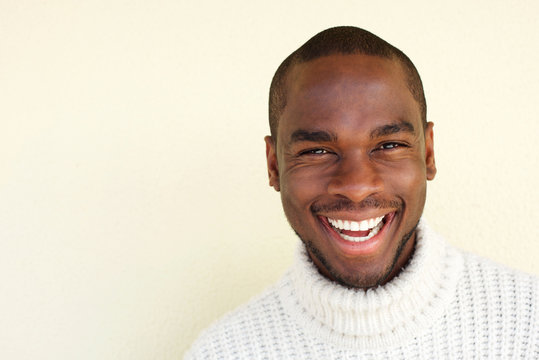 Close up happy young african american man laughing against light background