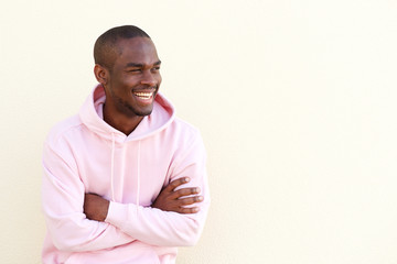 cheerful young black man posing with arms crossed by wall