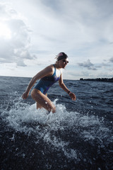 Young woman in swimsuit running in the water during triathlon competition