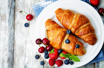 Croissants with fresh berries and mint leaves on a wood background