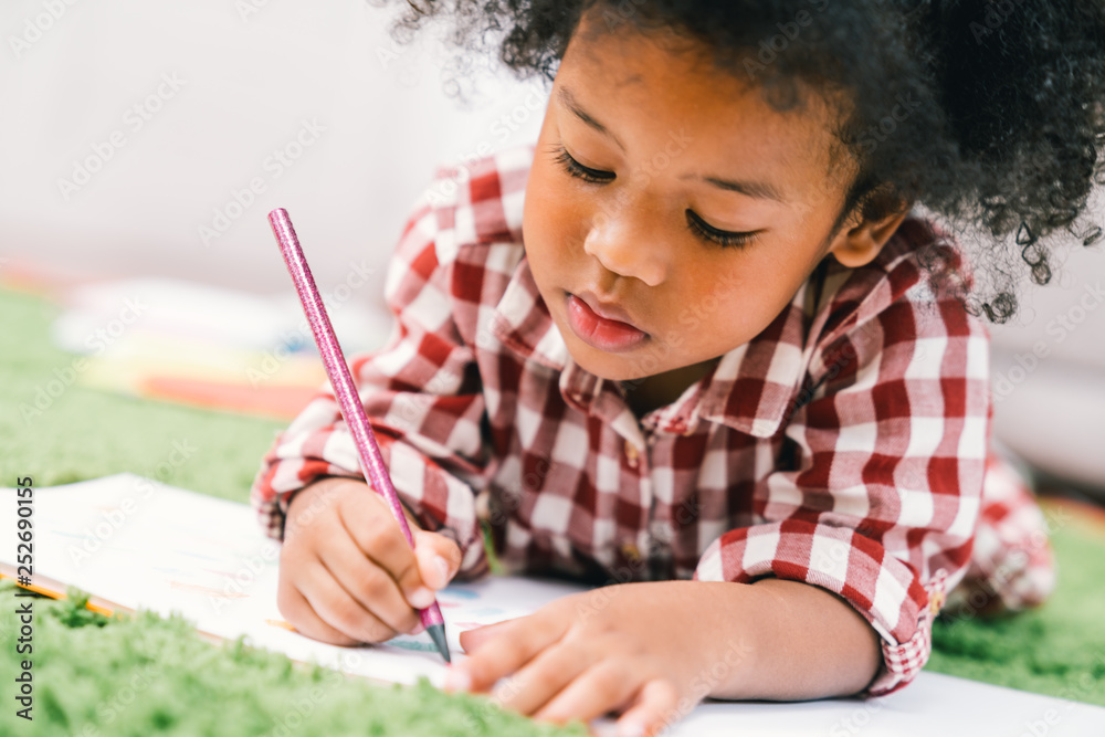 Wall mural Cute young African American kid girl drawing or painting with colored pencil. Kindergarten children education, back to school, or preschool child study at home concept