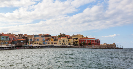 Obraz premium A panorama of the harbor city of Chania. View of the emarald sea, interesting landscapes, colorful houses, a coast view from the cafe. The Mediterranean Sea. A popular tourist resort in the Greece.