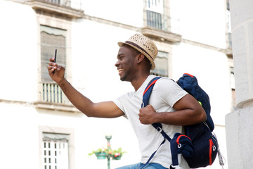 african american male tourist sitting outside with bag and mobile phone taking selfie