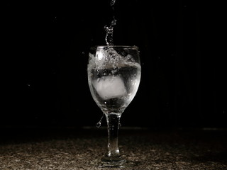 Frozen moving image. Ice falling on a glass with drink that spills and splashes.