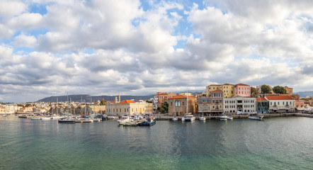 Fototapeta na wymiar A panorama of the seaport town Chania, the island of Crete, Greece. A harbor with wooden pantons, moored yachts, ships, boats. Colorful architecture of modern and old houses. Mountains on the horizon.