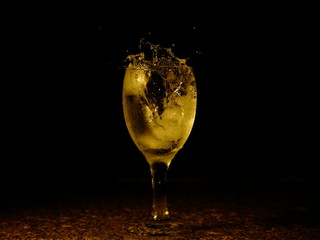 Frozen moving image. Ice falling on a glass with drink that spills and splashes.