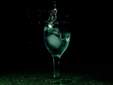 Frozen moving image. Ice falling on a glass with drink that spills and splashes.