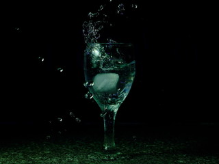 Frozen moving image. Ice falling on a glass with drink that spills and splashes.