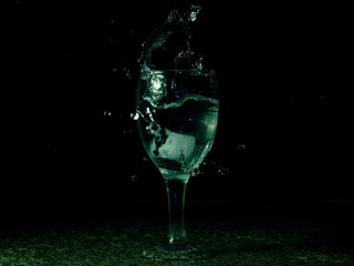 Frozen moving image. Ice falling on a glass with drink that spills and splashes.