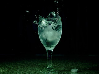 Frozen moving image. Ice falling on a glass with drink that spills and splashes.