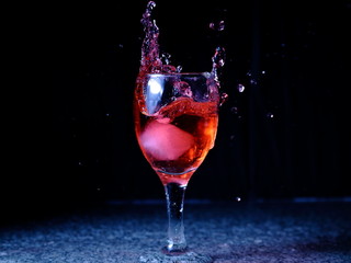 Frozen moving image. Ice falling on a glass with drink that spills and splashes.