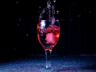 Frozen moving image. Ice falling on a glass with drink that spills and splashes.