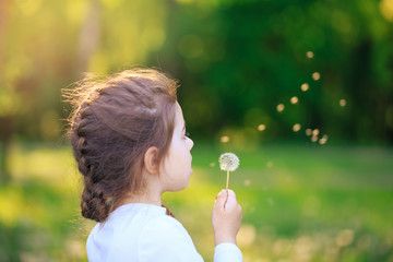 Cute little girl with dandelion flower is smiling in spring park. Happy cute kid having fun...