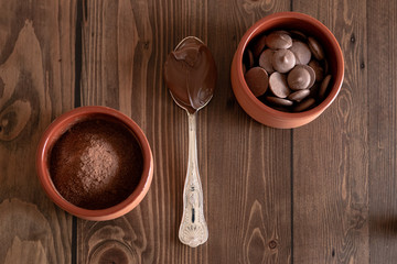 Chocolate powder, pieces and melted chocolate on a wooden background.