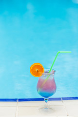 Glass with cocktail on the edge of resort swimming pool. Vacations concept.