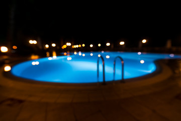 Illuminated swimming pool at night time. Grab bars ladder in the blue swimming pool at tropical resort.