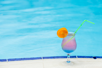 Glass with cocktail on the edge of resort swimming pool. Vacations concept.