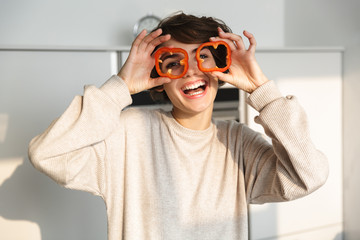 Cheerful girl holding sliced capsicum at her face