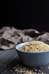 Rolled oats in ceramic bowl on dark wooden background, copy space