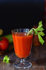 Fresh tomato juice in a glass goblet with a celery sprig and a tomato twig in the background in a low key, vertical