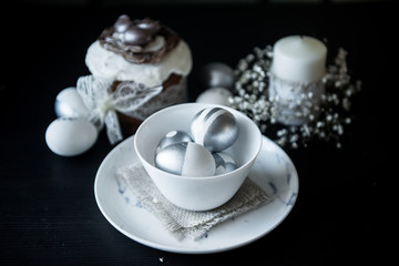 Traditional Easter cake with silver painted eggs, candles on a black background. Selective focus