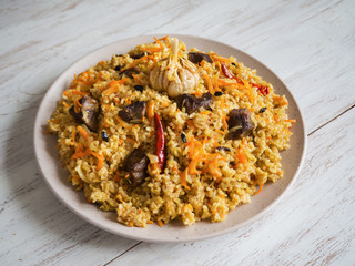 Uzbek pilaf in a plate on a white wooden table. 