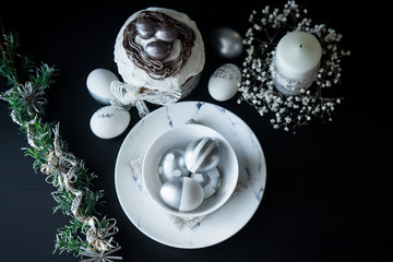 Traditional Easter cake with silver painted eggs, candles and willow on a black background. Selective focus