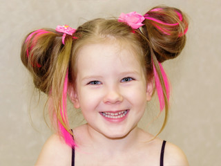 Closeup portrait of a cute smiling child. Face of little happy pretty girl smiles on white background wall. Baby having fun with her pink hair.