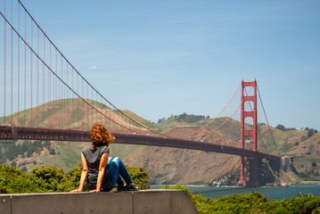 Young woman is watching Golden Gate bridge from a tourist point near the bridge in San Francisco,...
